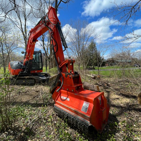Red excavator clearing invasive brush while preparing a native wildflower meadow site