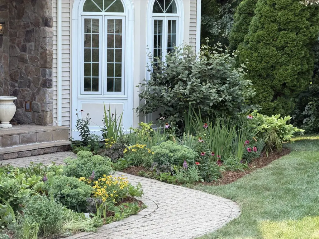 Perennial foundation garden with flowering plants and a curved walkway beside a home